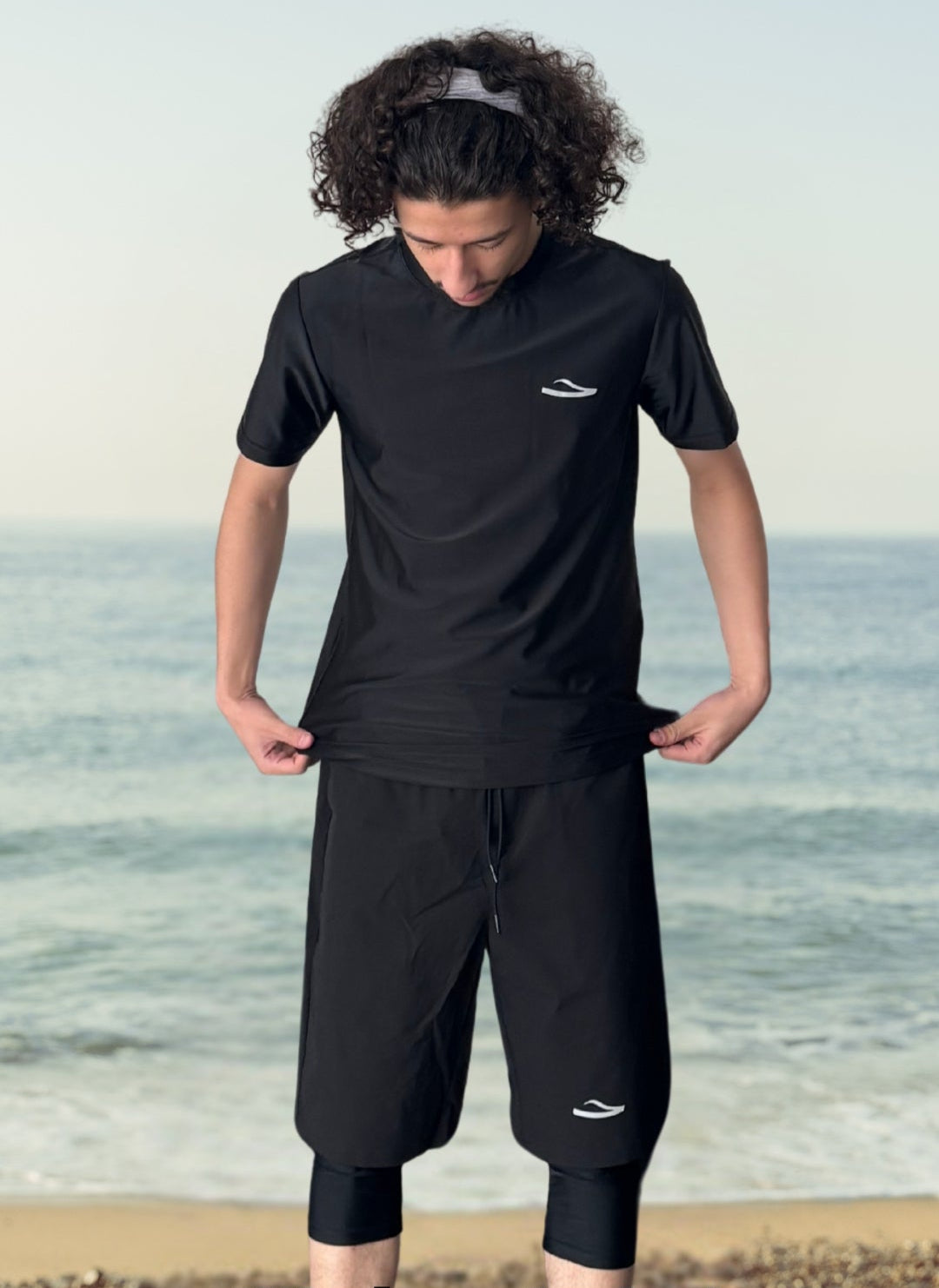 Homme portant un short de bain musulman noir pudique avec legging intégré et un t-shirt de bain noir sur la plage
